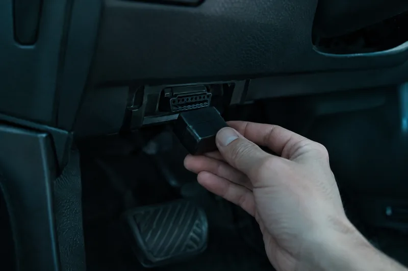 Рука вставляє маленький OBD-адаптер у роз’єм під кермом